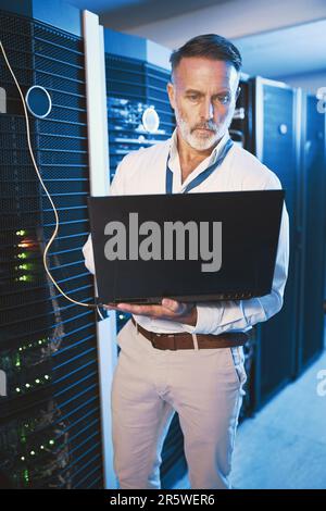 Switching between systems for a quicker connection. a mature man using a laptop while working in a server room. Stock Photo