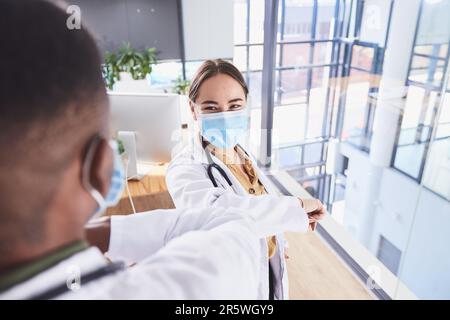 The new handshake. two unrecognizable doctors wearing masks and elbow bumping while standing in the hospital. Stock Photo