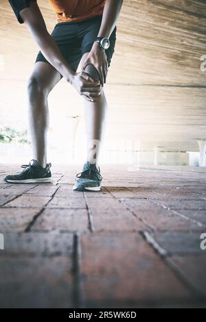 Dont let pain out-run you. a man experiencing joint pain while working out against an urban background. Stock Photo