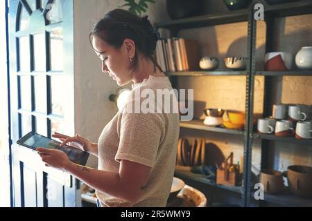 Business never stops. an attractive young business owner standing alone in her pottery studio and using a tablet. Stock Photo