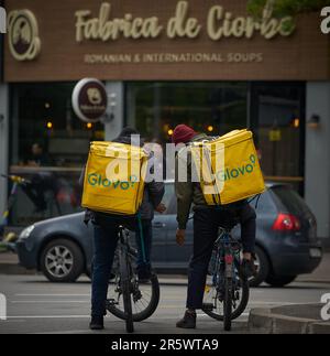 Bucharest, Romania - 9th May, 2023: Two Glovo food delivery couriers, workers of foreign origin, most likely from South Asia, delivers food in Buchare Stock Photo