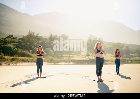 You get more out than you put in. three young women practicing yoga on the beach. Stock Photo