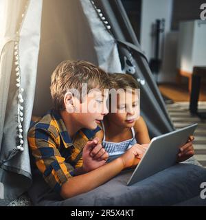 Siblings having fun on the wifi. an adorable little boy and girl using a tablet together while chilling in a homemade tent in the living room at home. Stock Photo