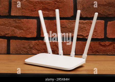 New white Wi-Fi router on wooden table near brick wall Stock Photo