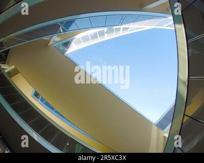 Image from below of a modern architecture building with a complex shape and pedestrian walkways. Reflective windows and the light blue sky in the back Stock Photo