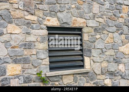 Window of a house closed with black wooden shutters. Old, ancient wood window with blind or shutters. Stone home facade. Old wooden slat shutter windo Stock Photo