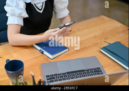 Close-up image of a businesswoman or female office worker using her smartphone at her desk. Stock Photo