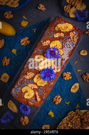 Banana bread with chocolate, banana chips and nuts, decorated with cornflowers, vegan, food photography Stock Photo