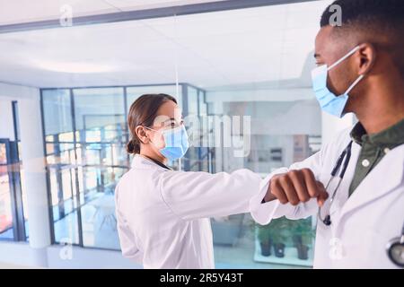 Greetings to flatten the curve. two unrecognizable doctors wearing masks and elbow bumping while standing in the hospital. Stock Photo