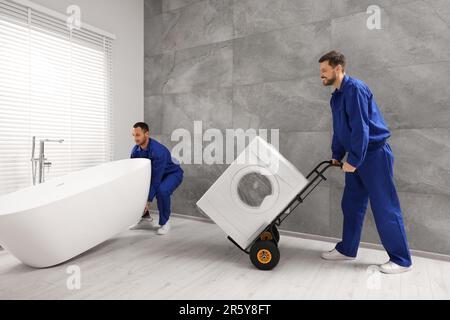 Male movers with bathtub and washing machine in bathroom. New house Stock Photo