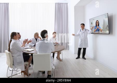 Lecture with online participant. Doctors in meeting room. Using tv for videoconference Stock Photo