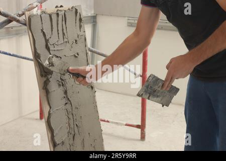 Worker spreading adhesive mix over tile with spatula, closeup Stock Photo