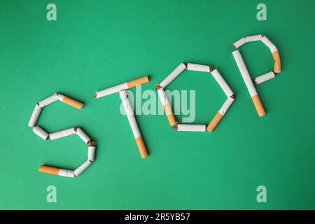 Word Stop made of broken cigarettes on green background, flat lay. Stop smoking concept Stock Photo