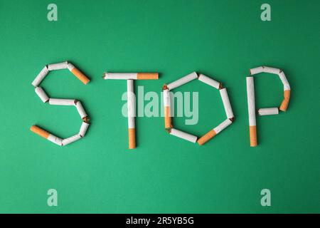 Word Stop made of broken cigarettes on green background, flat lay. Stop smoking concept Stock Photo
