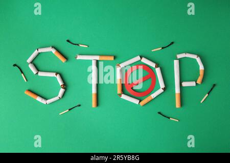Word Stop made of broken cigarettes, prohibition sign and burnt matches on green background, flat lay. Stop smoking concept Stock Photo