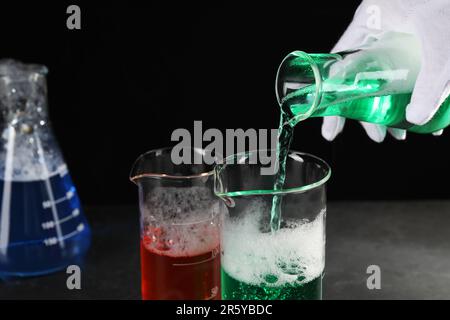 Scientist working with laboratory glassware at black table, closeup. Chemical reaction Stock Photo
