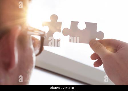Businessman hands connecting puzzle pieces representing the merging of two companies or joint venture, partnership, Mergers and acquisition concept. Stock Photo