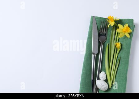 Cutlery set, Easter eggs and narcissuses on white background, top view with space for text. Festive table setting Stock Photo