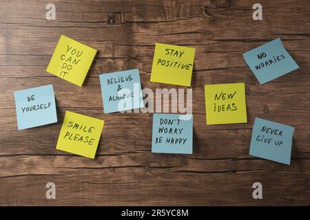 Paper notes with life-affirming phrases on wooden table, flat lay Stock Photo