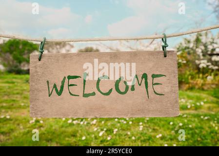 Welcome card. Wooden board with word hanging on rope in countryside Stock Photo