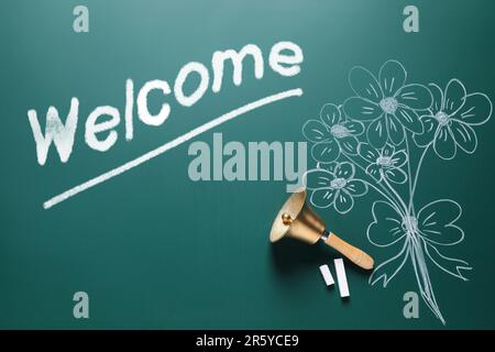 Welcome card. Golden bell, chalk, word and drawn flowers on green board, flat lay Stock Photo