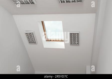 Skylight roof window and lamps on slanted ceiling in attic room, low angle view Stock Photo