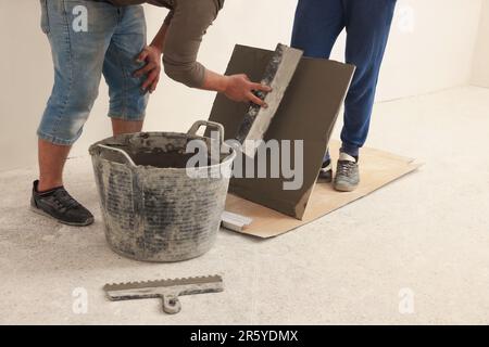 Worker spreading adhesive mix over tile with spatula, closeup Stock Photo