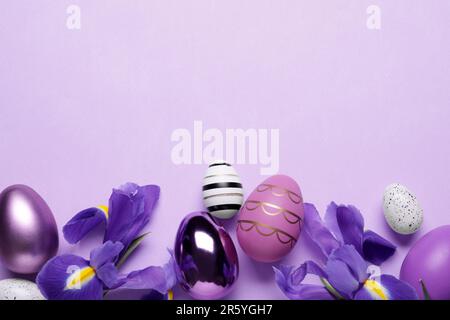 Flat lay composition with iris flowers and beautifully painted eggs on violet background, space for text. Easter celebration Stock Photo