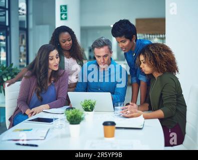 We just need to add to the design. a group of designers gathering around a man using a laptop in a meeting. Stock Photo
