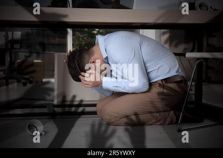 Paranoid individual. Scared man hiding under desk and having delusion as hands reaching for him Stock Photo