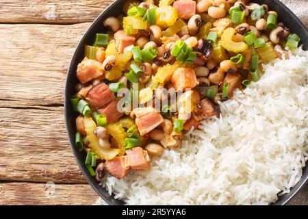 Hoppin John of black-eyed peas, bacon, sausages, vegetables and scallions with rice closeup on the plate on the wooden table. Horizontal top view from Stock Photo