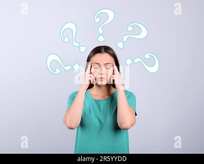 Amnesia concept. Woman surrounded by question marks trying to remember something on light background Stock Photo