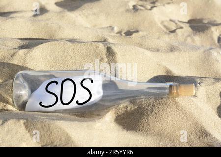 Glass bottle with SOS message on sand outdoors Stock Photo