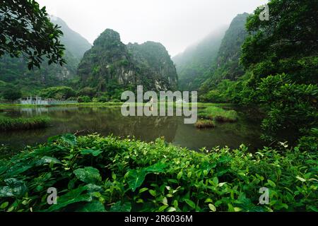 Graveyard settled between lush green limestone hills covered in fog at a lake, Ninh Binh, Vietnam Stock Photo