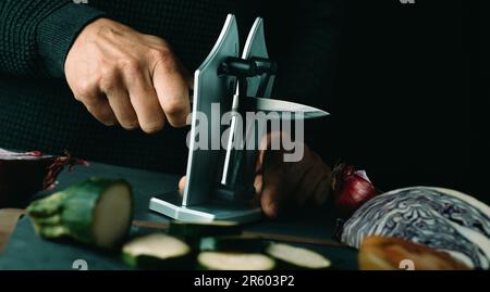man sharpening a kitchen knife with a desktop sharpener on a table, in a panoramic format to use as web banner or header Stock Photo