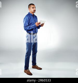 Technology holds so many possibilities. Studio shot of a young businessman using his tablet against a grey background. Stock Photo