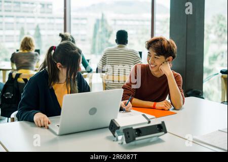 Diverse students sitting at table with laptop Stock Photo