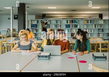 Group of multiethnic students discussing in library with laptop Stock Photo