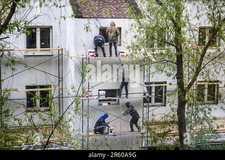 Unrecognizable migrant workers are plastering the outer wall of the building, on the scaffolding. Stock Photo