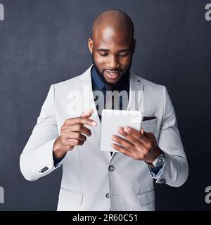 Business related info on tap. Studio shot of a businessman using a digital tablet against a gray background. Stock Photo