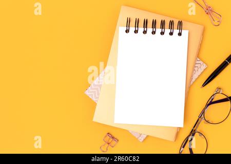 Workspace with empty notepad mock up and gold colored stationery on a yellow background. Place for text. Stock Photo