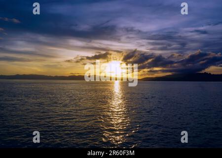 Sunset over the sea in Komodo National Park, Indonesia, sun reflects in sea, clouds on the horizon Stock Photo