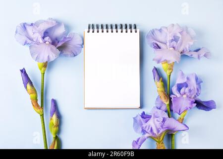 Notebook with clean page with purple flowers irises on orange background. Flat lay style. Stock Photo