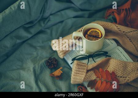 Dark atmospheric photo with open book, cup of lemon tea, cozy warm sweater, eyeglasses Stock Photo