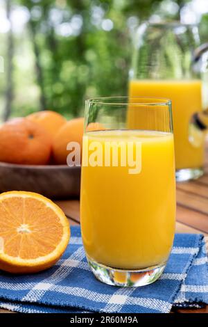 Glass of orange juice and oranges outdoors on a wooden table with nature background Stock Photo