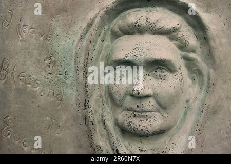 A portrait of anolder woman wearing a head scarf and cast in a copper metal wall. Stock Photo