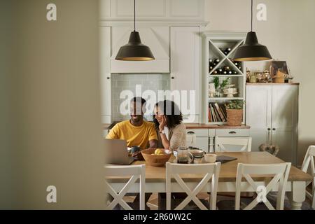 Smiling young multiethnic couple using a laptop during breakfast at home Stock Photo