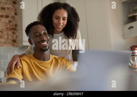 Smiling young multiethnic couple using a laptop together in their kitchen Stock Photo