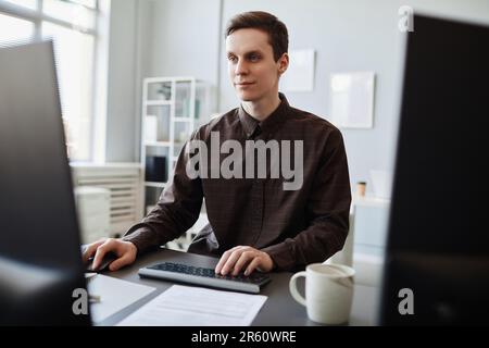 Portrait of smiling young man using computer in clean office workplace, copy space Stock Photo