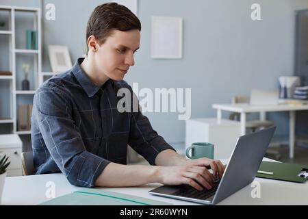 Side view portrait of young man using laptop in minimal office setting and smiling, copy space Stock Photo